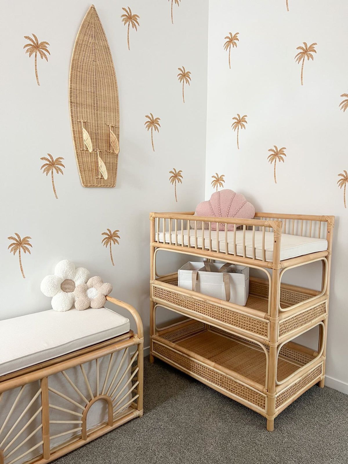 A changing table and storage bench in a nursery wall with palm tree decals and a woven surfboard decoration hang.