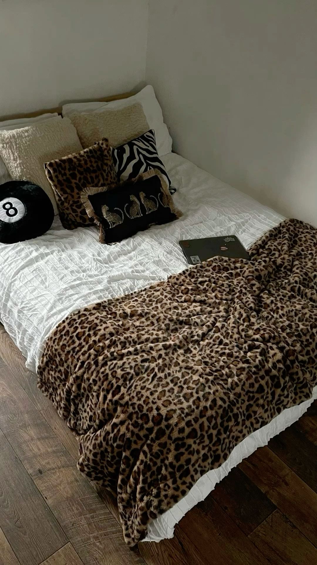 A bed with white bedding, a leopard print throw blanket, and an assortment of pillows, including one with a leopard print…
