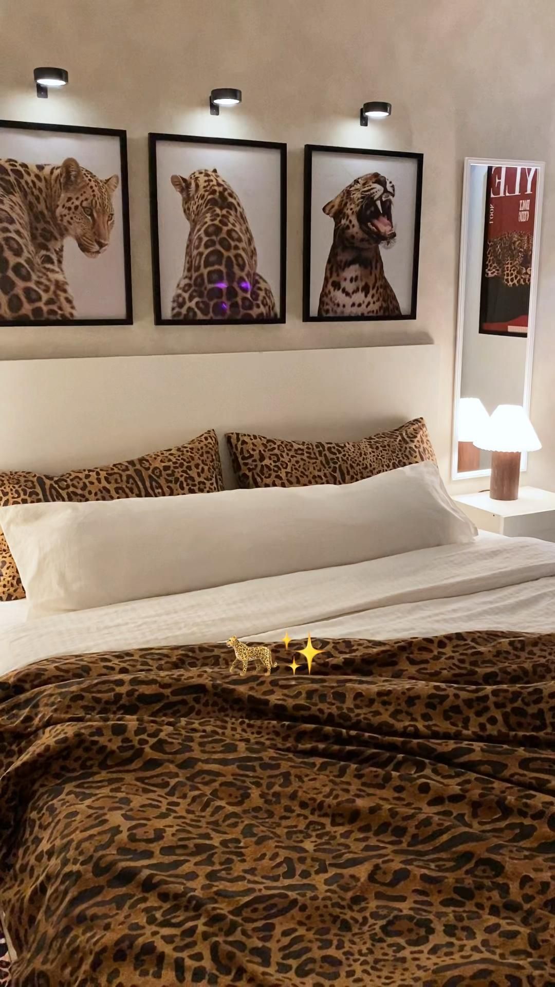 A bedroom with a white headboard, white sheets, and leopard print throw blanket and pillow shams.