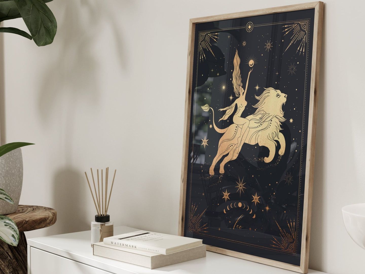 A framed art print featuring a golden lion and a figure on a dark, star-filled background, leaning against a white dresser.