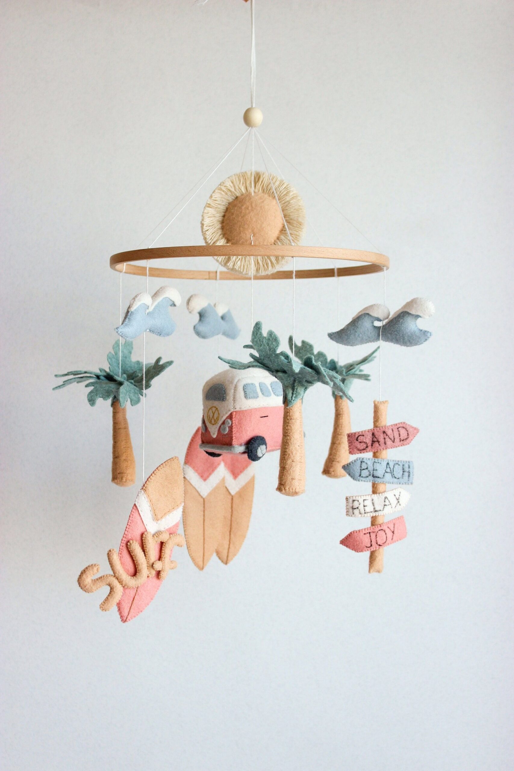 Felt mobile with a sun, clouds, palm trees, a pink and white camper van, surfboards, and a directional sign.