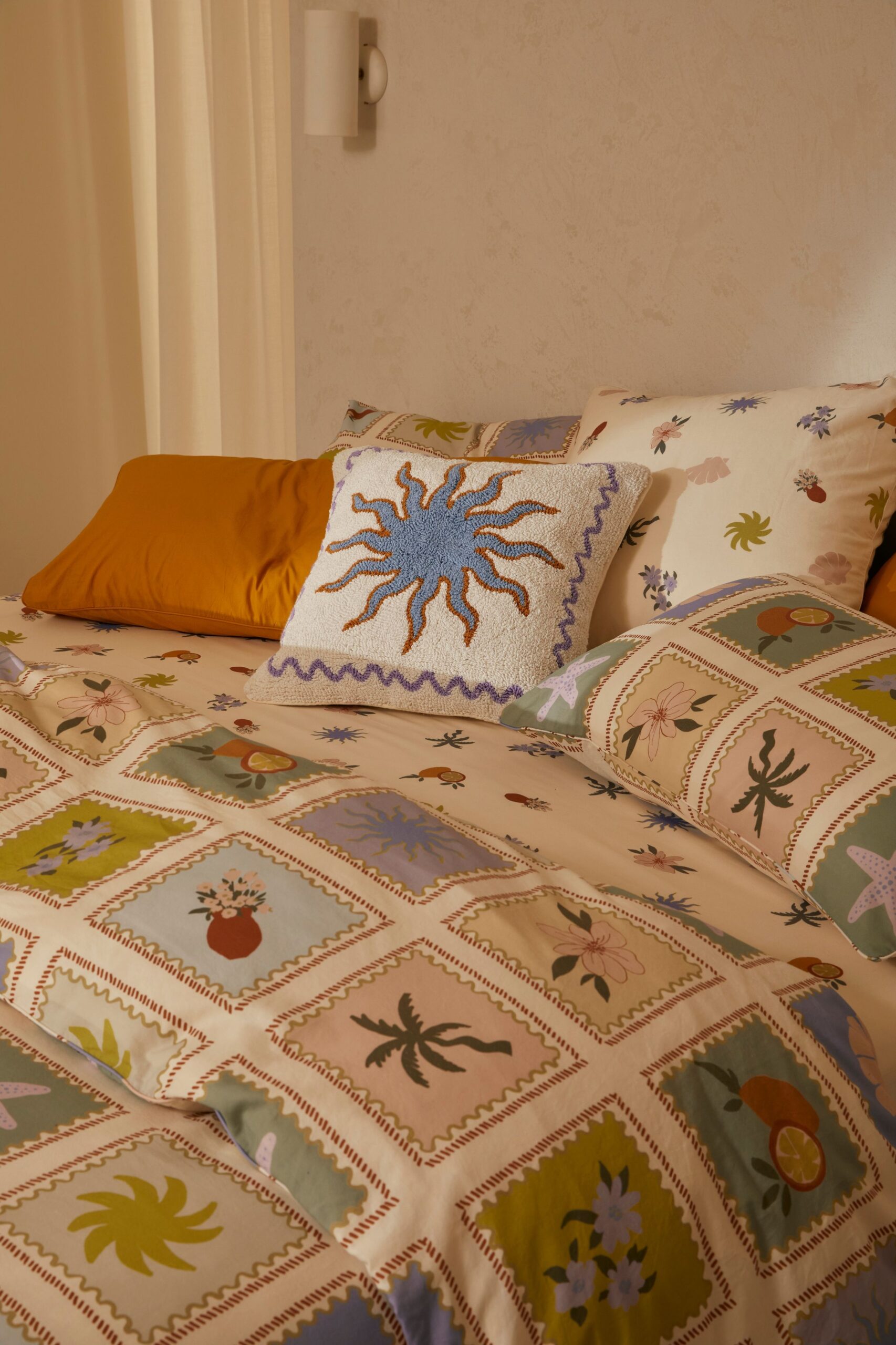 Close-up of a bed with white sheets and pillowcases printed with varied designs inside squares, and one solid yellow pillow…