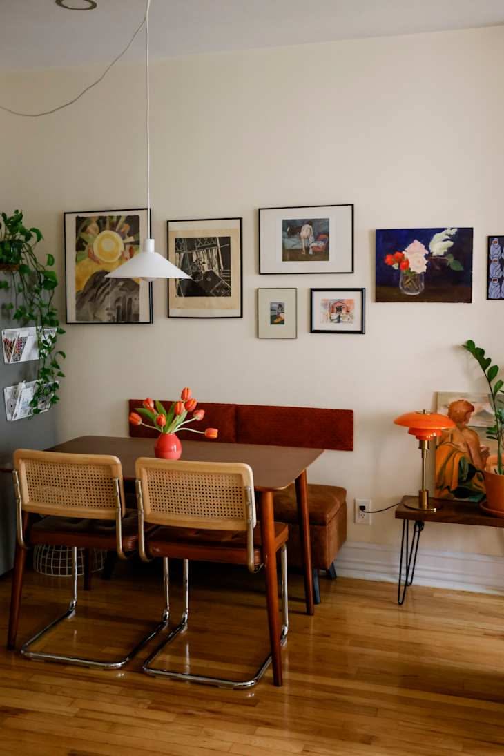 A dining table with two chairs on one side and a red upholstered banquette with brown base against a white wall.