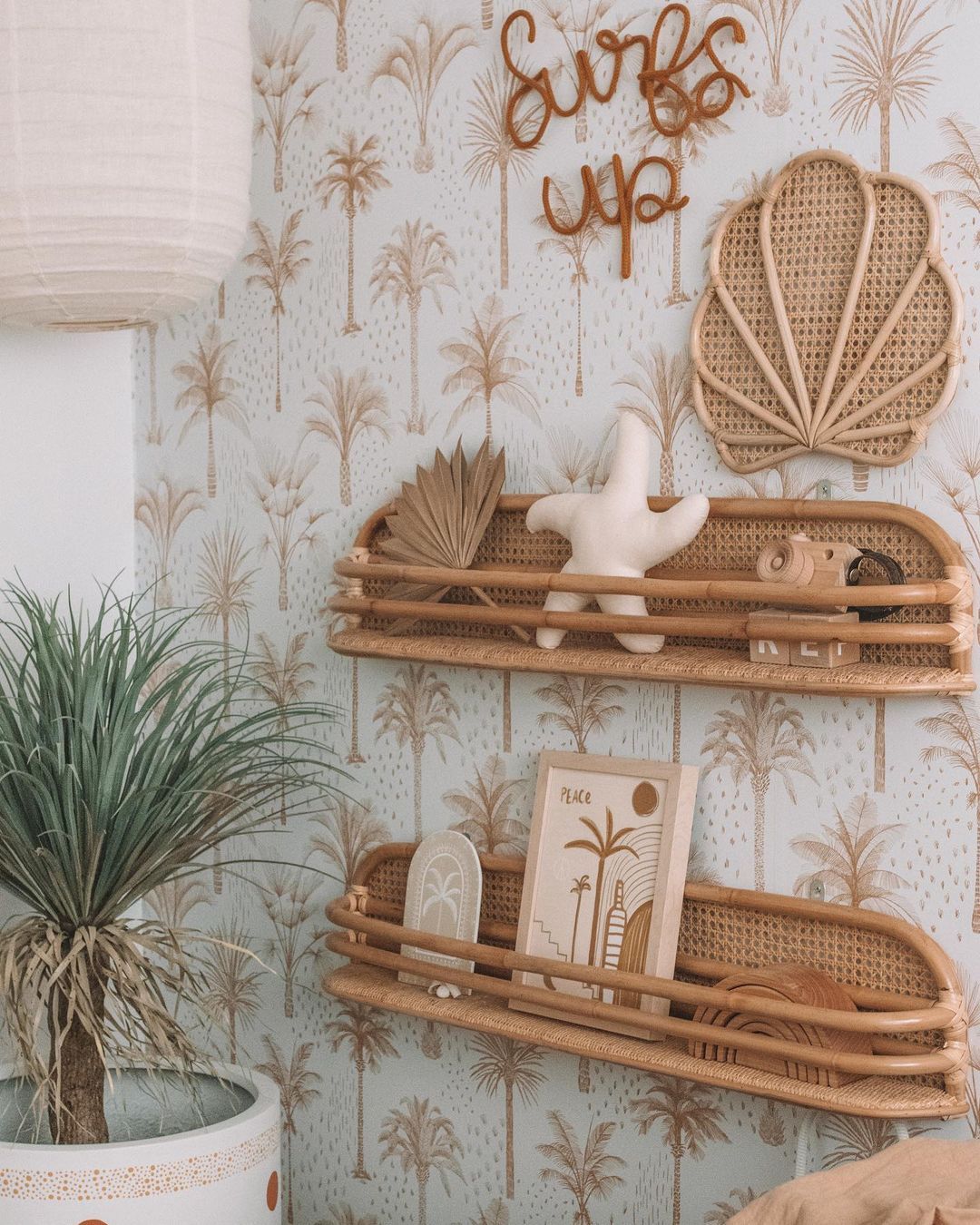 Palm frond wallpaper, rattan shelves with decor, and a houseplant create a summer-themed nursery corner.