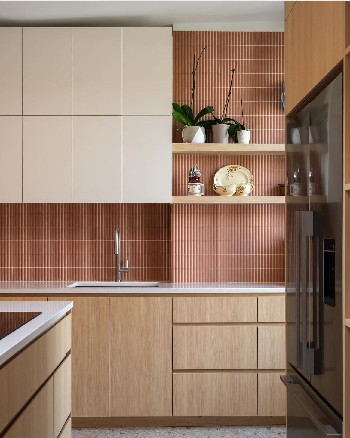 Modern kitchen with rose-colored vertical tile backsplash, light wood lower cabinets, and white upper cabinets.