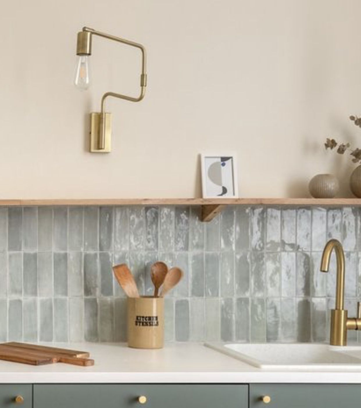Kitchen counter with light blue iridescent vertical subway tiles as a backsplash, brass faucet, and olive green cabinets.