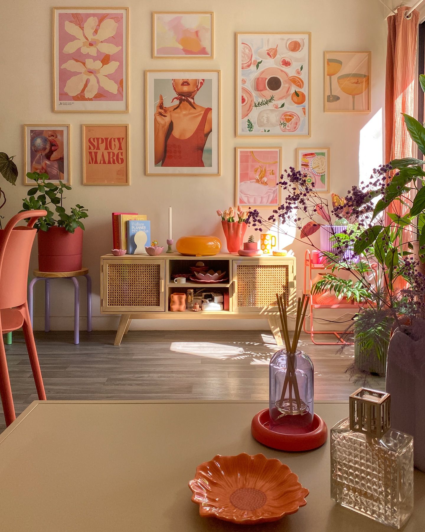 Living room with gallery wall and a light wood cabinet filled with colorful decorative objects, including dishes, candles…