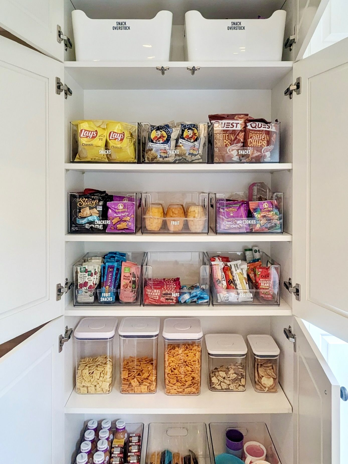 A pantry cabinet stocked with various snacks, organized into clear bins and containers by type.