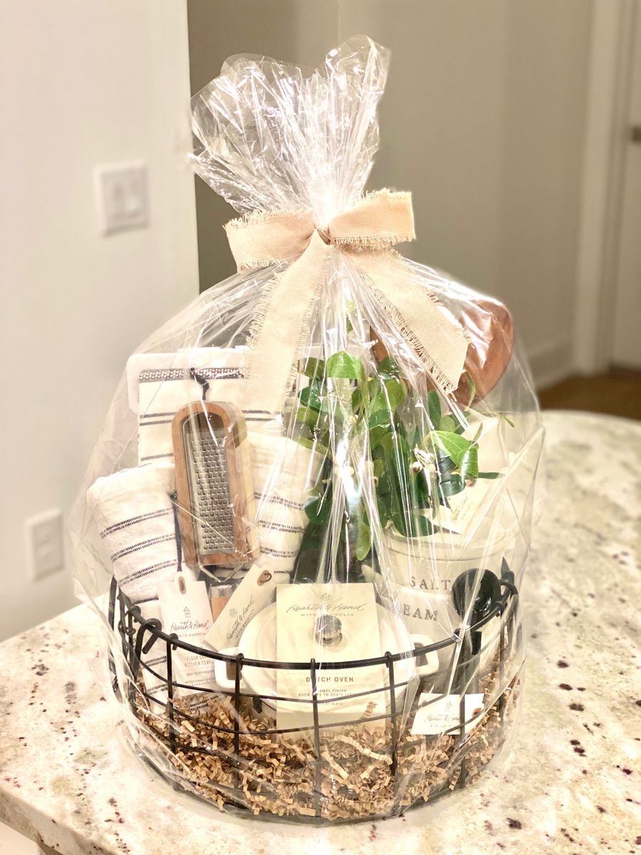 Gift basket filled with kitchen essentials, including towels, a grater, a small plant, and ceramic containers, wrapped in…