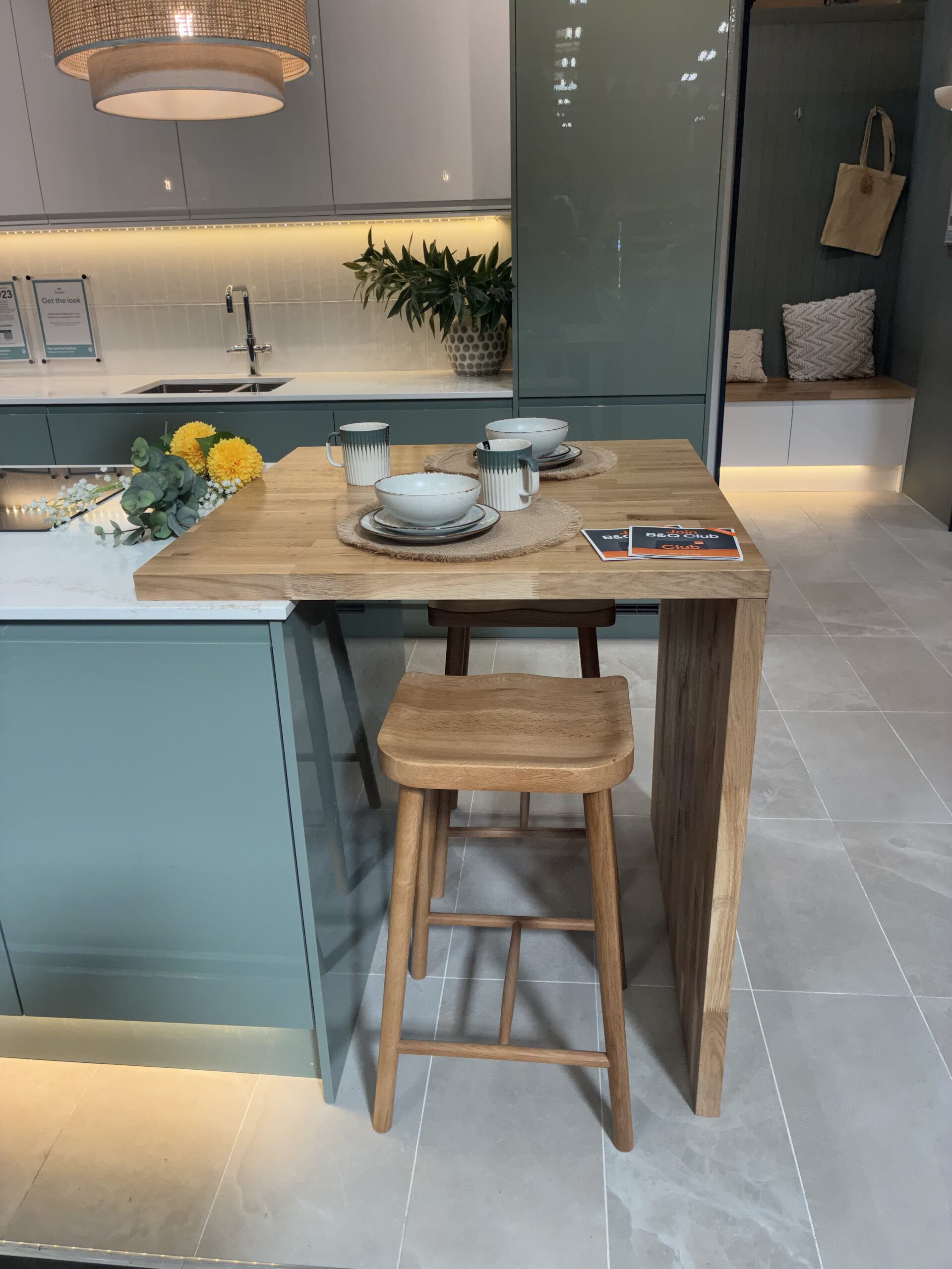 Wooden breakfast bar extended from a kitchen counter with two stools underneath, set with dishes.
