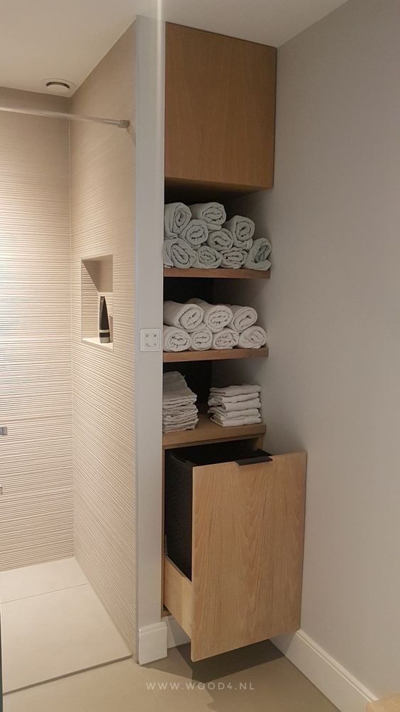Tall, light wood built-in cabinet with open shelves holding rolled and folded towels, next to a tiled shower.