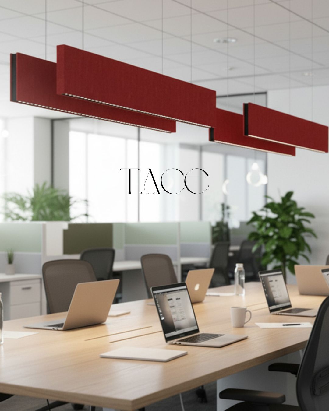 Red linear acoustic light fixtures hang over a modern wooden table with laptops in an open office.