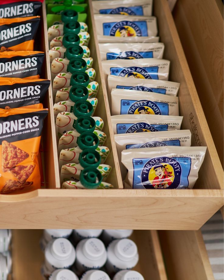 Close-up of a wooden pull-out drawer with slanted dividers, organizing snack bags and apple sauce pouches.