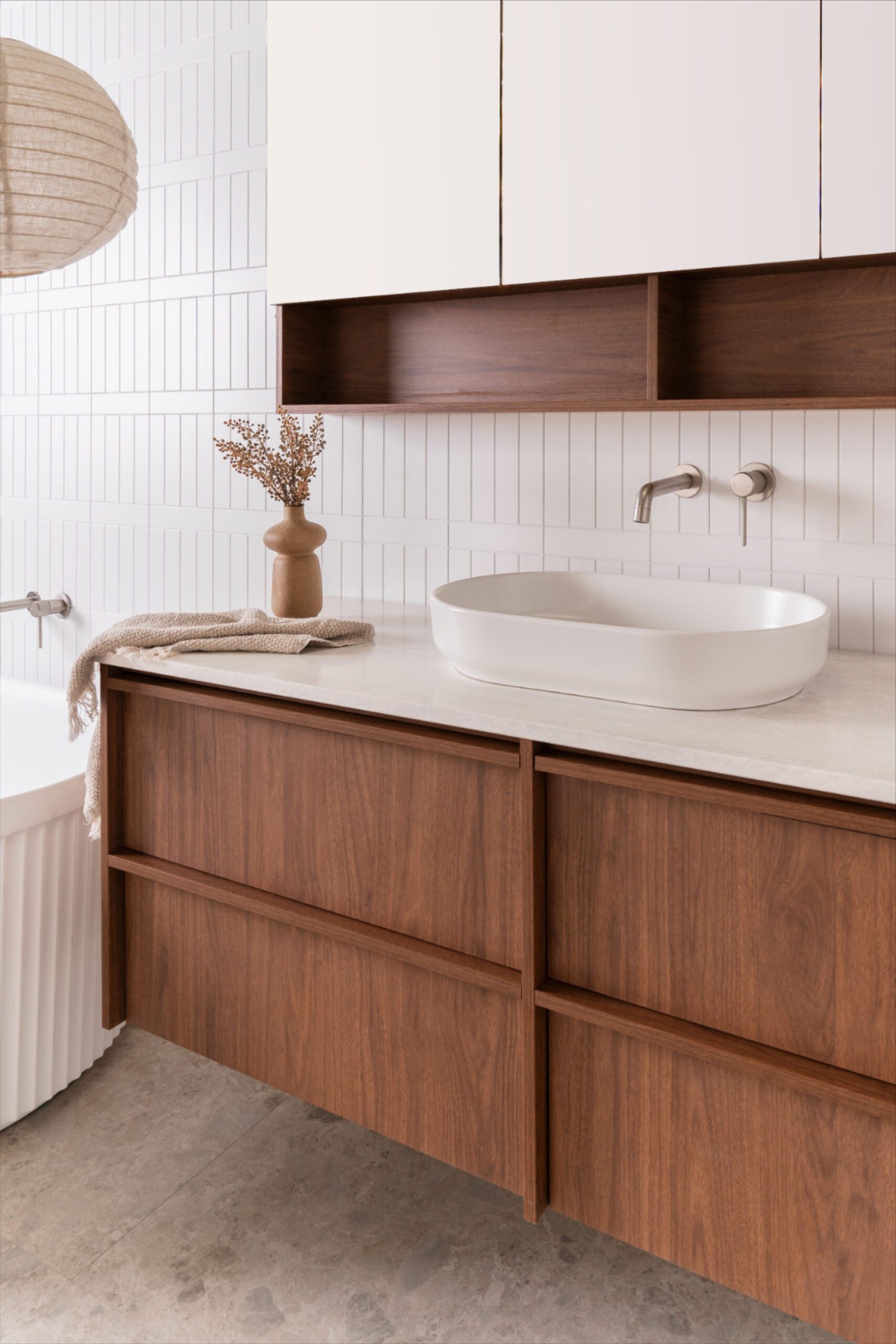 A bathroom vanity with warm brown wood cabinets, a white countertop, and a white oval vessel sink.