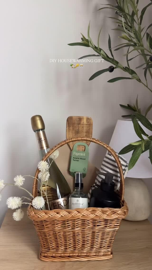 Wicker basket containing a bottle of sparkling wine, a wood turner, a room spray, a soap dispenser, and a striped towel.