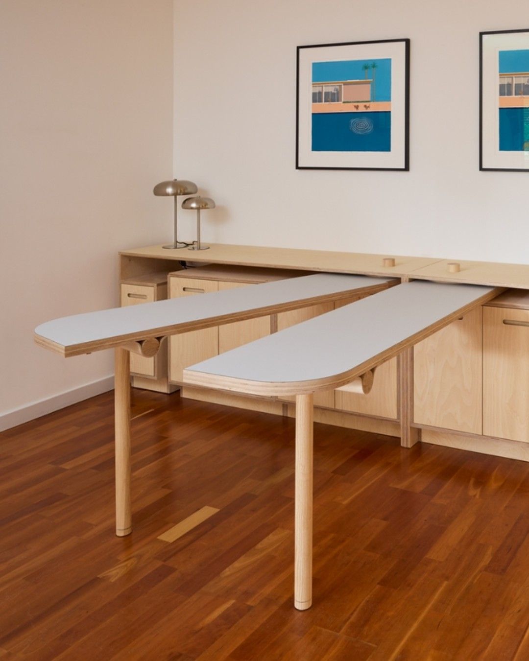 Two light wood tables, each with one rounded end, pulled out from under a light wood cabinet system.