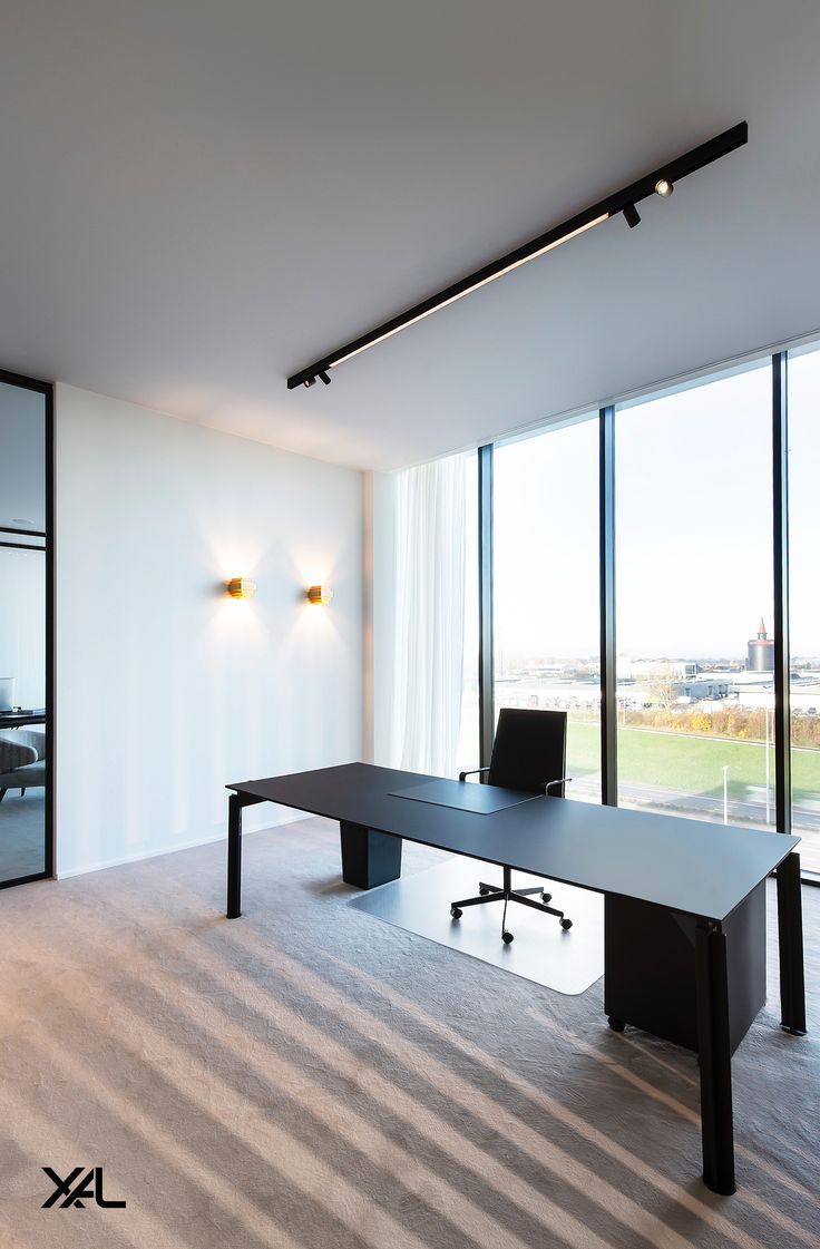 Modern home office with a black desk, office chair, large window, and linear track lighting on the ceiling