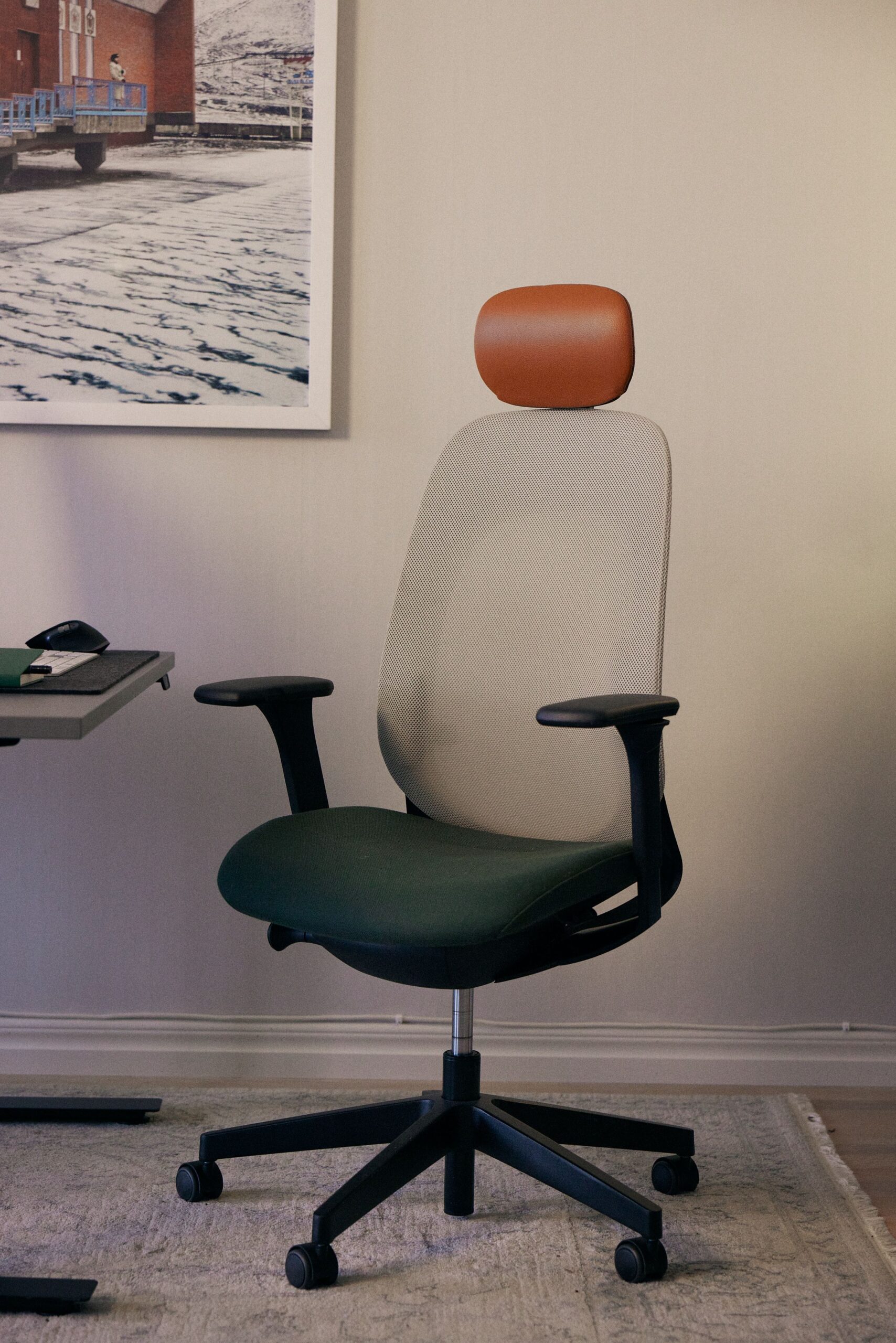 Ergonomic office chair with dark green seat, light mesh back, and brown headrest, next to a desk