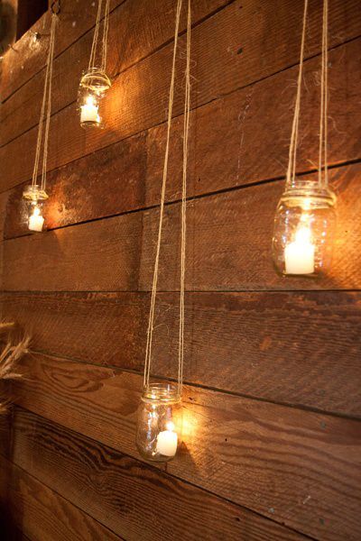 Mason jar lanterns with glowing candles hanging by twine against a warm wooden wall
