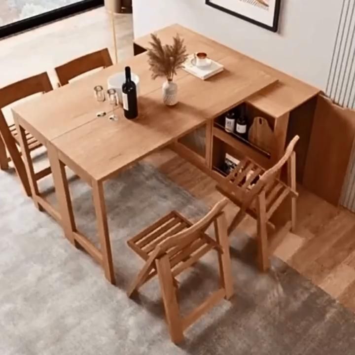 Light wood dining table with an expandable top and built-in shelving units, surrounded by folding chairs.