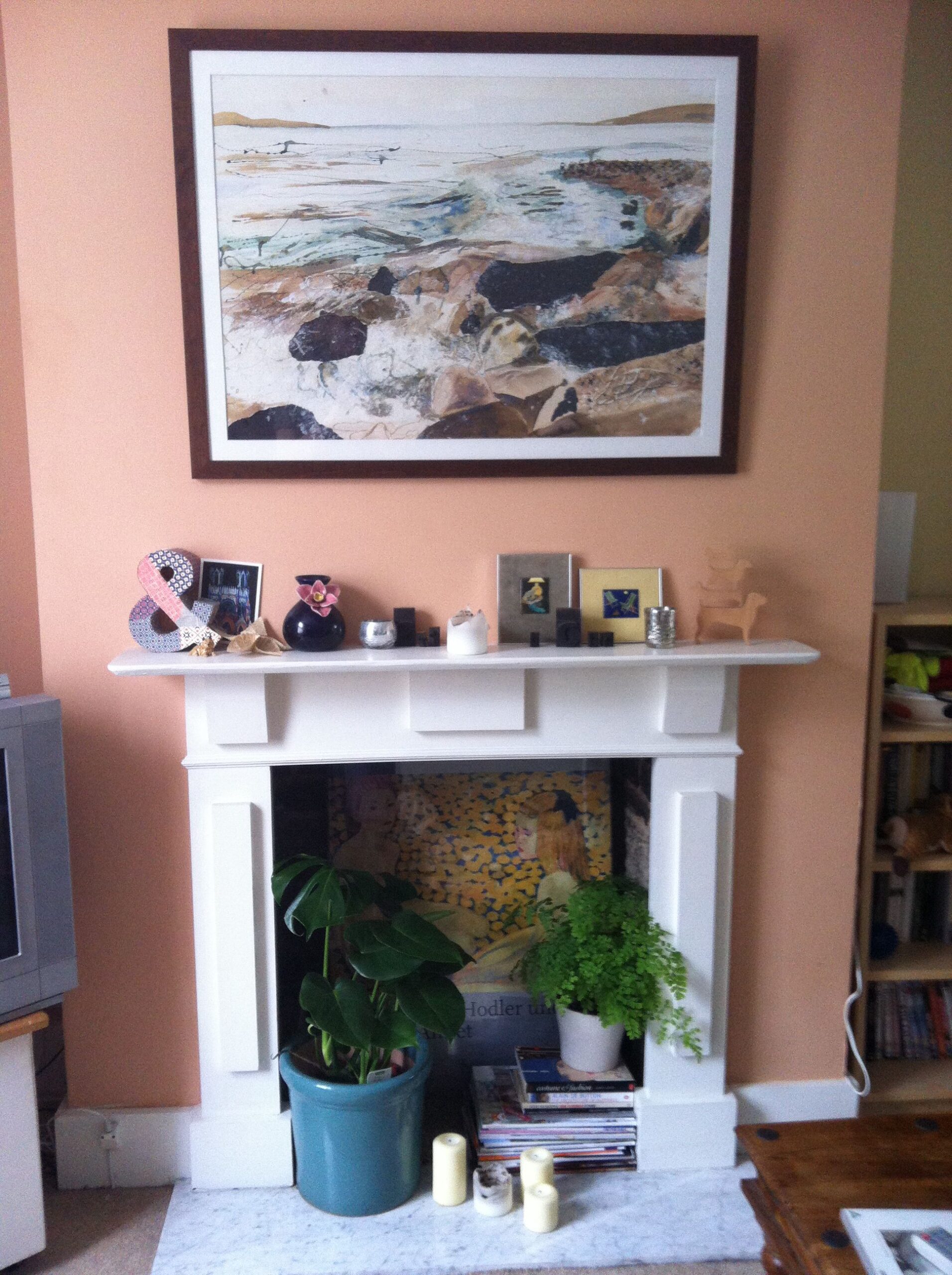 Decorative fireplace filled with a large potted houseplant, a smaller potted fern, and several candles
