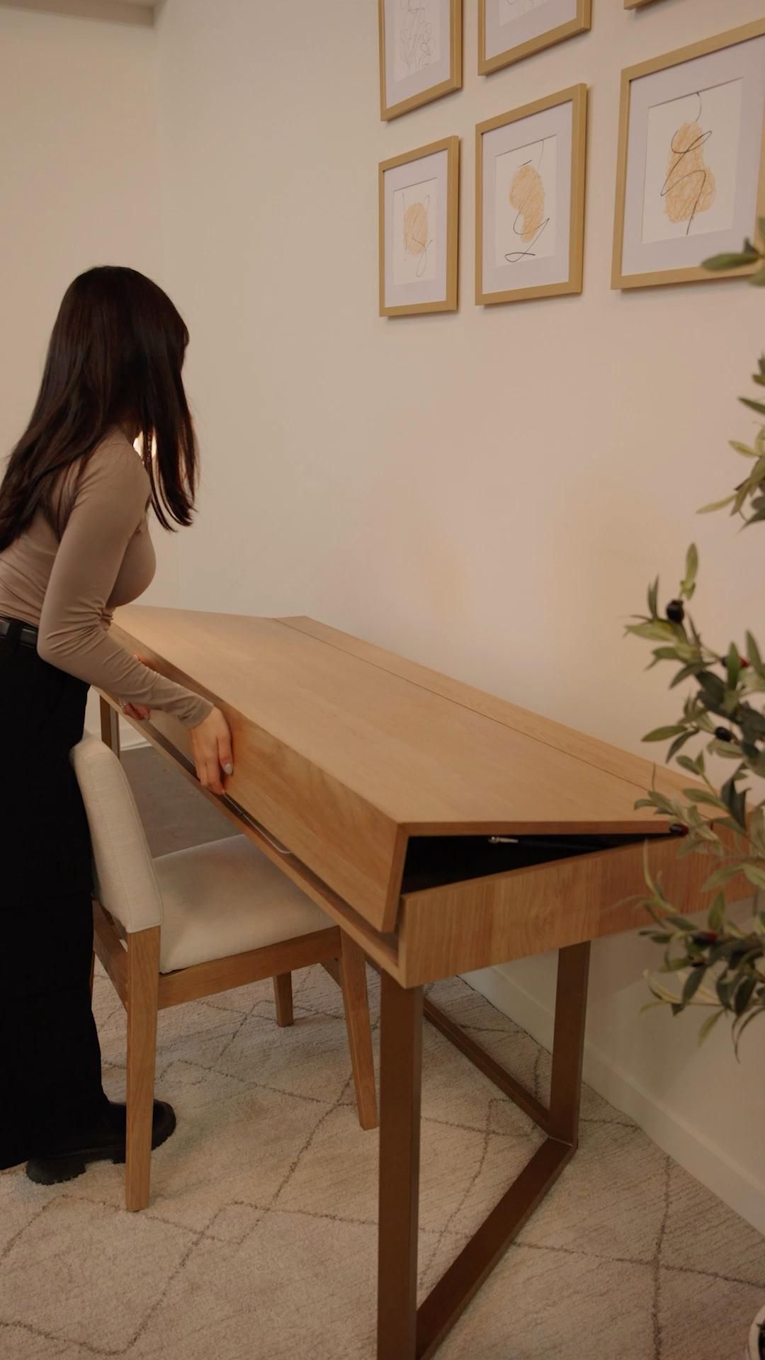 Person opening a wooden desk with a hinged top, revealing an internal storage compartment or work surface.