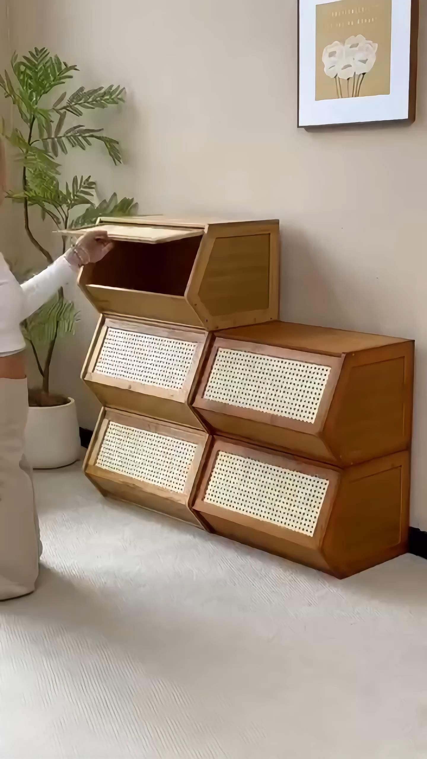 Person opening the top compartment of a stack of wooden storage bins with woven cane fronts