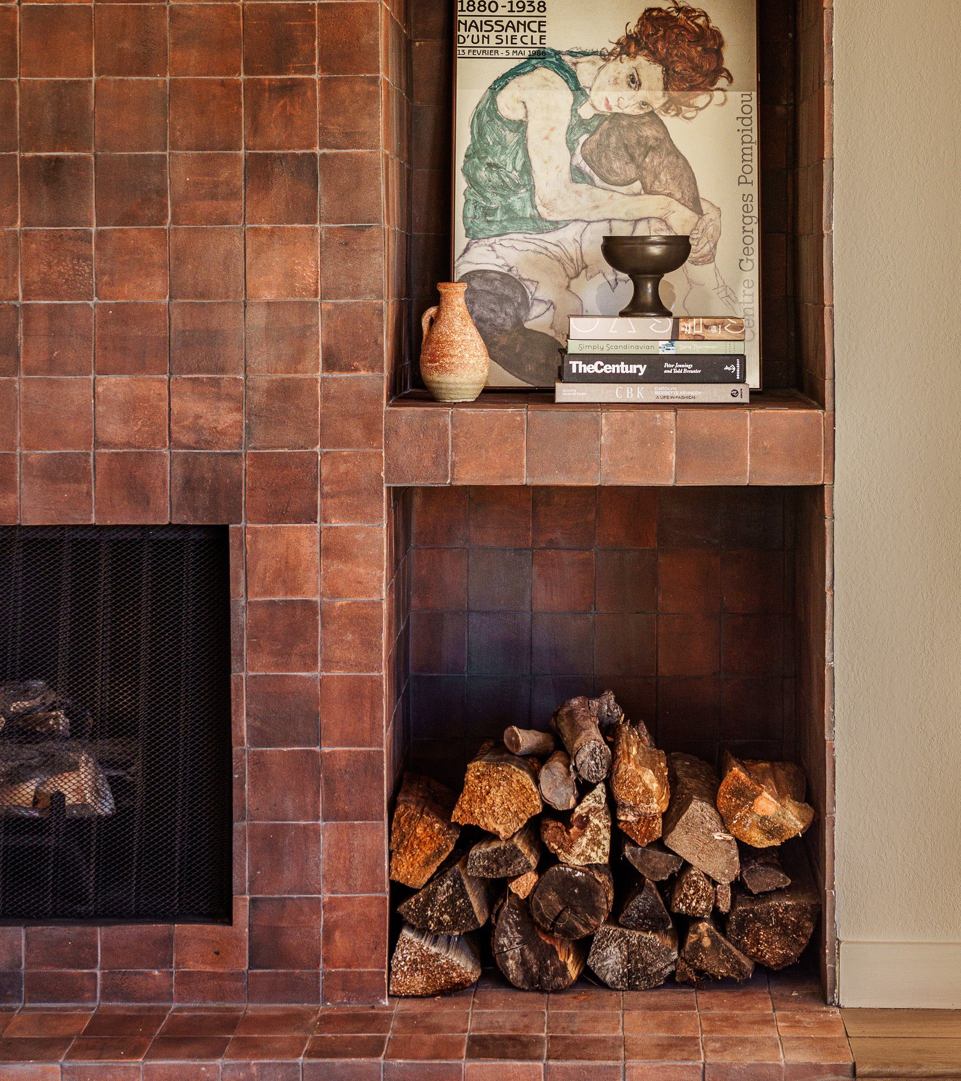 Terracotta square tile wall with a small arched fireplace opening and candles inside.