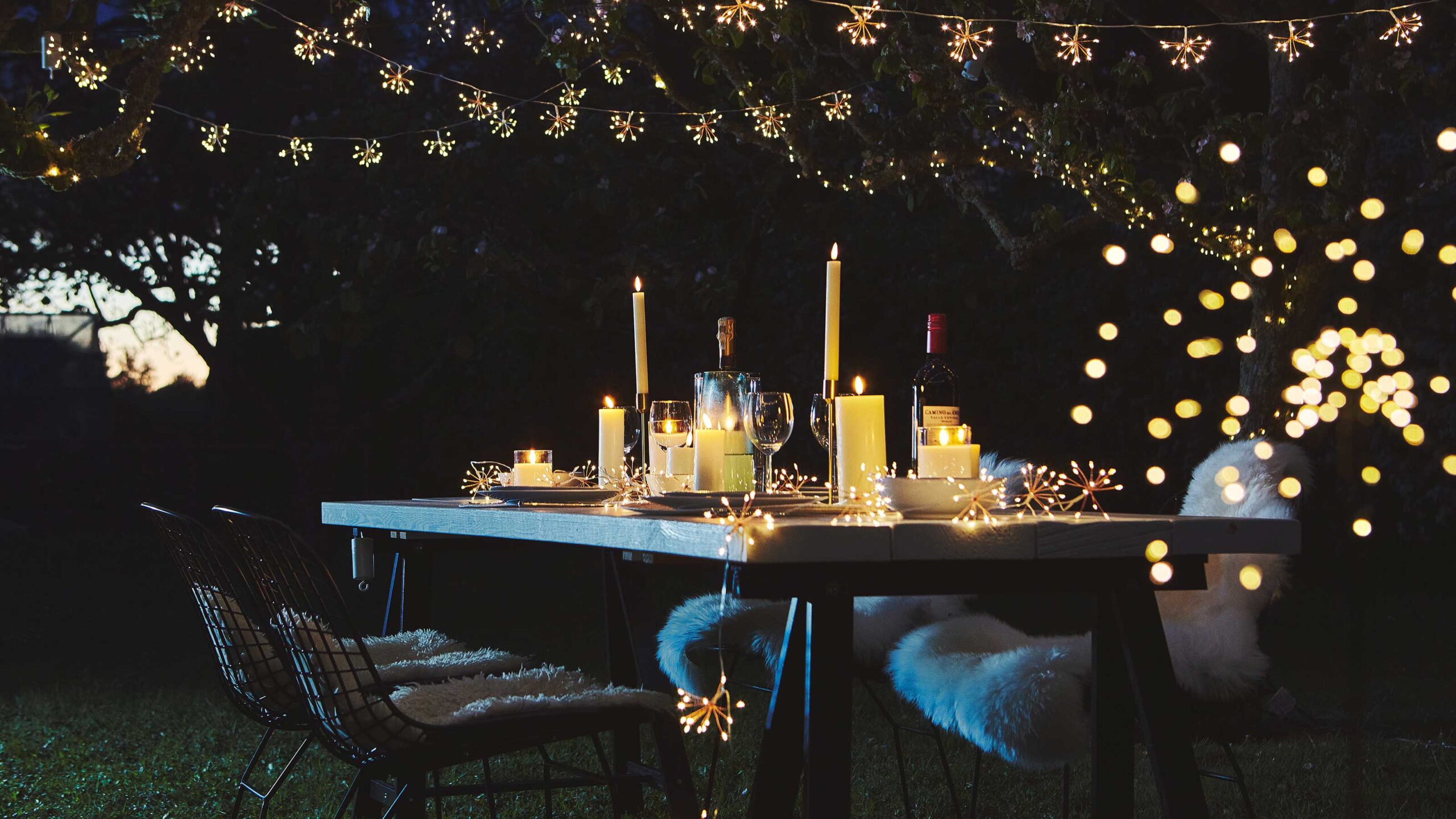 Outdoor patio table lit by hanging string lights and small table lamps