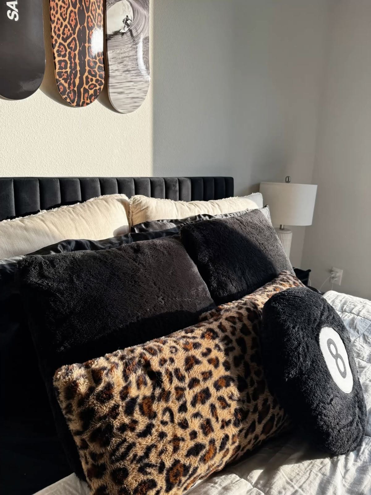 Close-up of a bed with black velvet headboard, cream, black faux fur, and leopard print pillows.