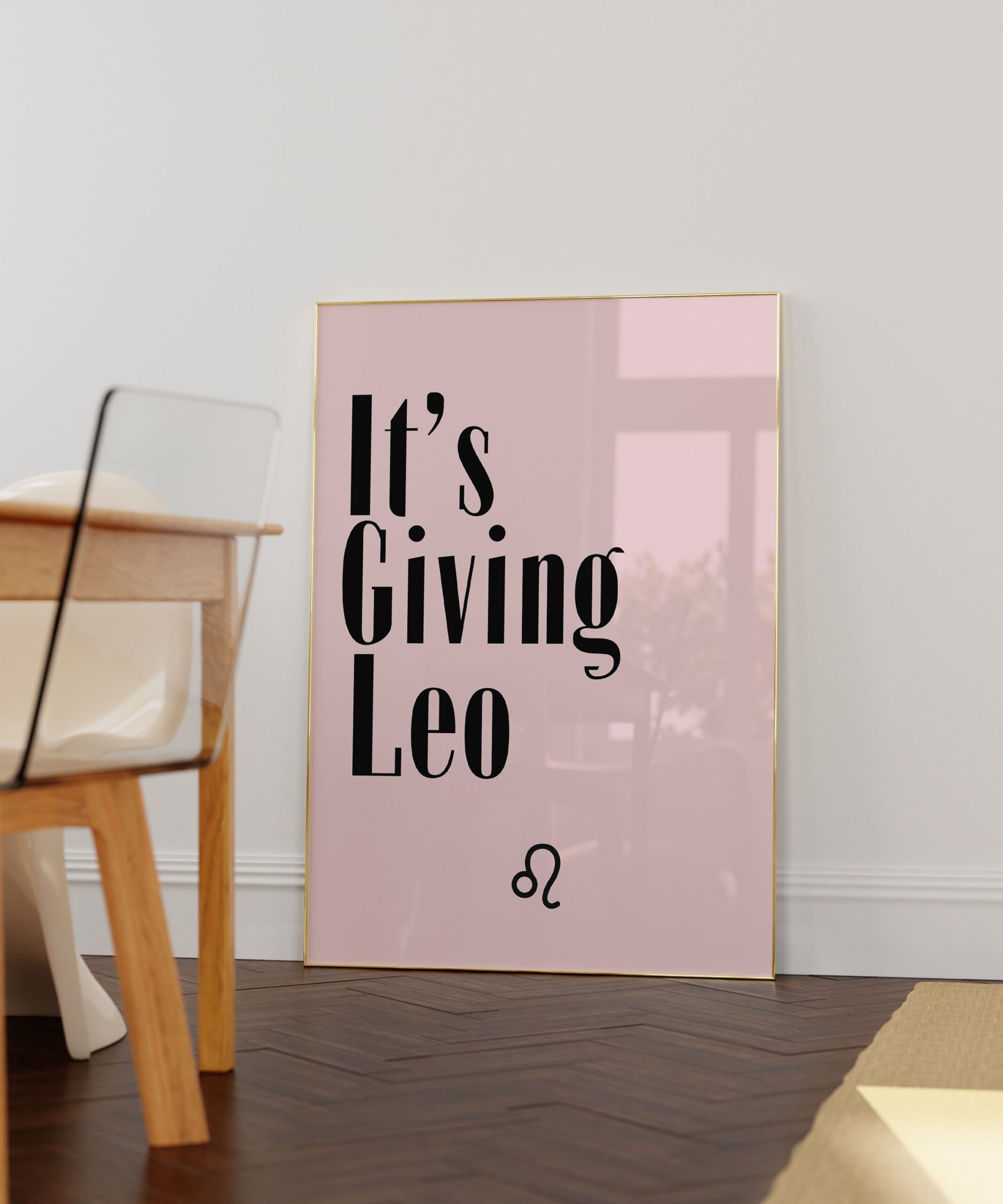 Pink framed wall art with the words "It's Giving Leo" and the Leo zodiac symbol in black text, leaning against a white wall.