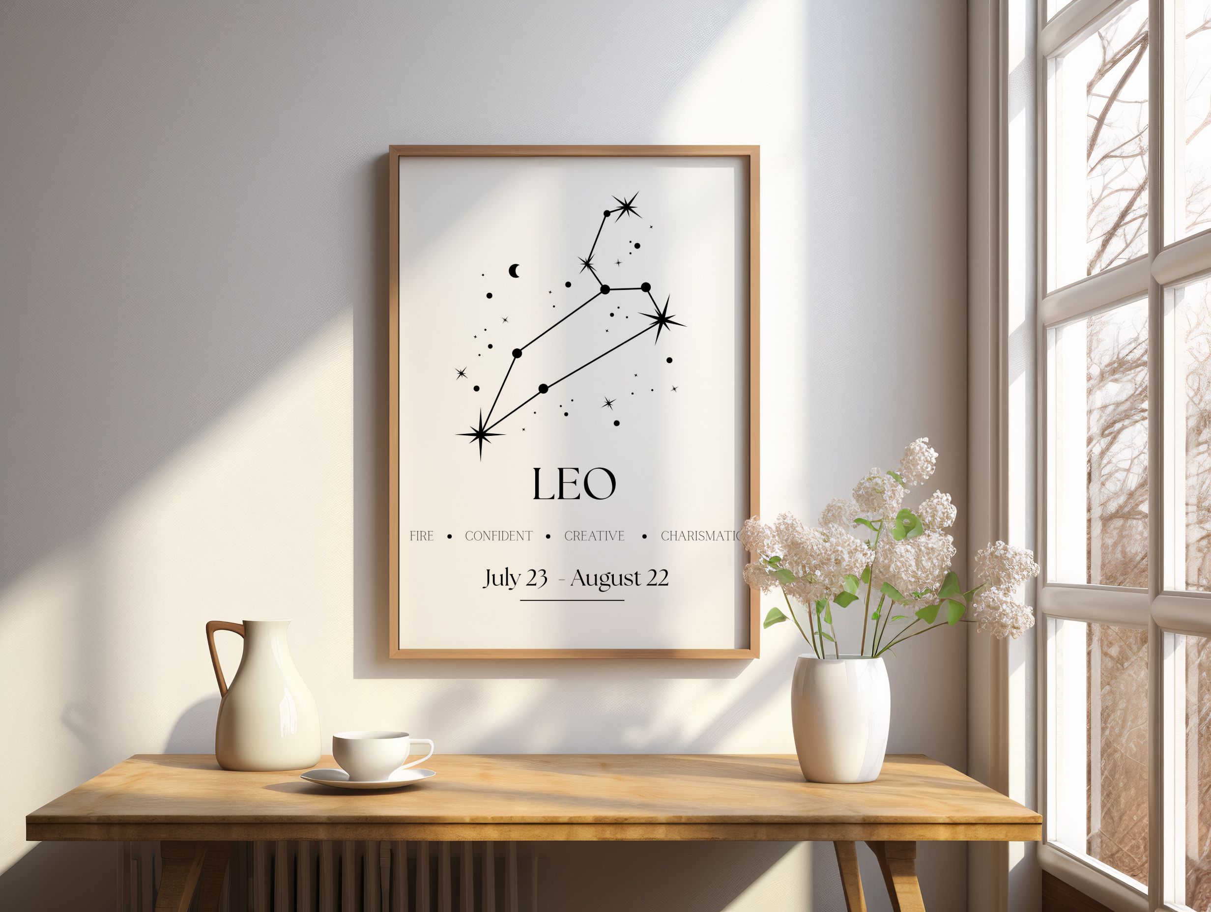 Black and white Leo constellation wall art hanging above a light wood desk with a white pitcher, coffee cup, and vase of…