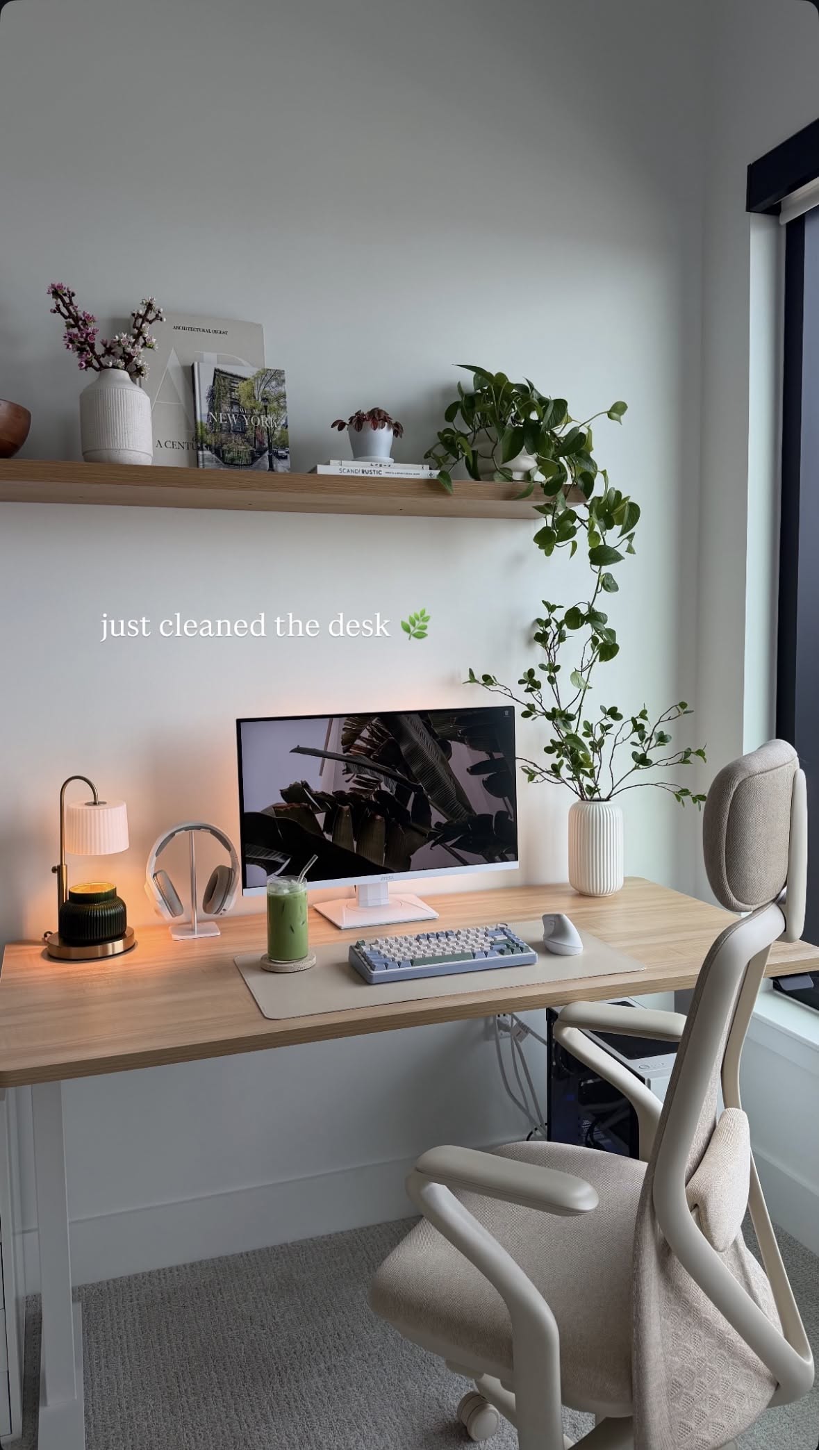 An illuminated brass and white pleated table lamp sits next to a computer monitor on a wooden desk.