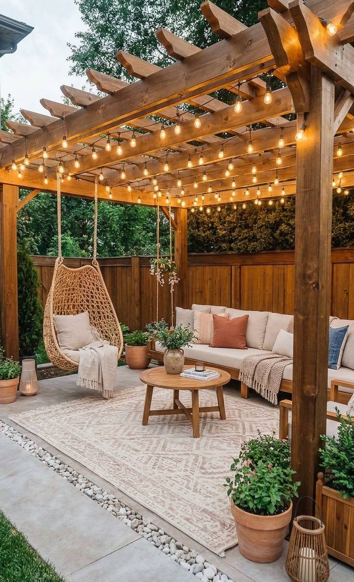 Pergola with string lights over a patio with outdoor sofa and hanging egg chair, and potted plants