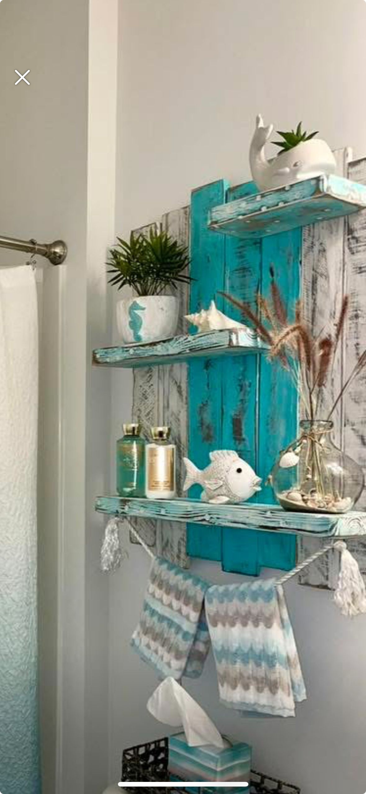 Decorative shelving unit in a bathroom, adorned with coastal themed items like a whale planter, seashells, and rustic jars.
