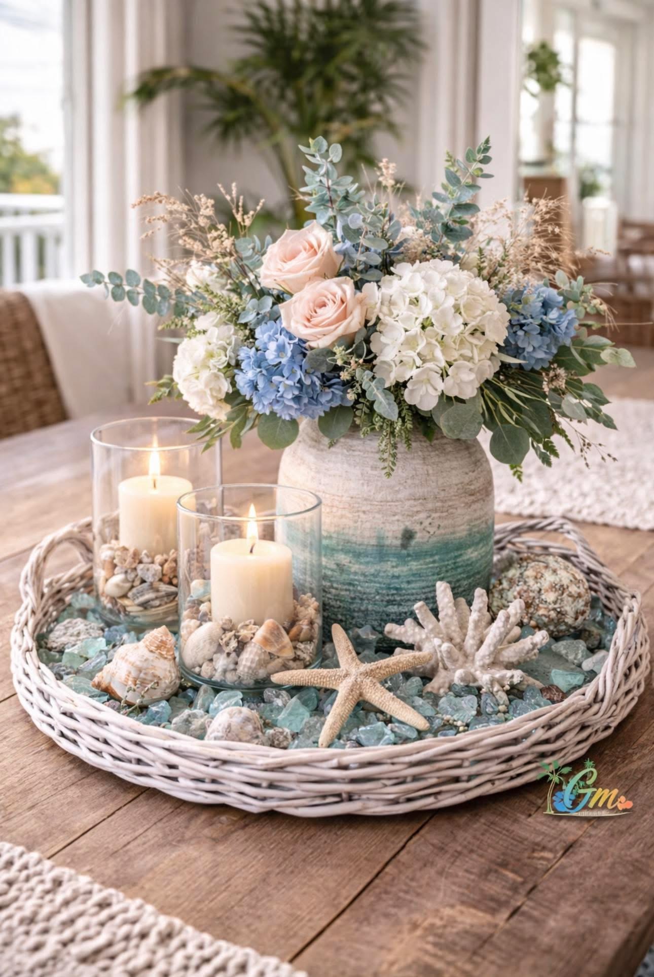 Decorative woven tray with candles, shells, starfish, and coral surrounding a vase of hydrangeas and roses.