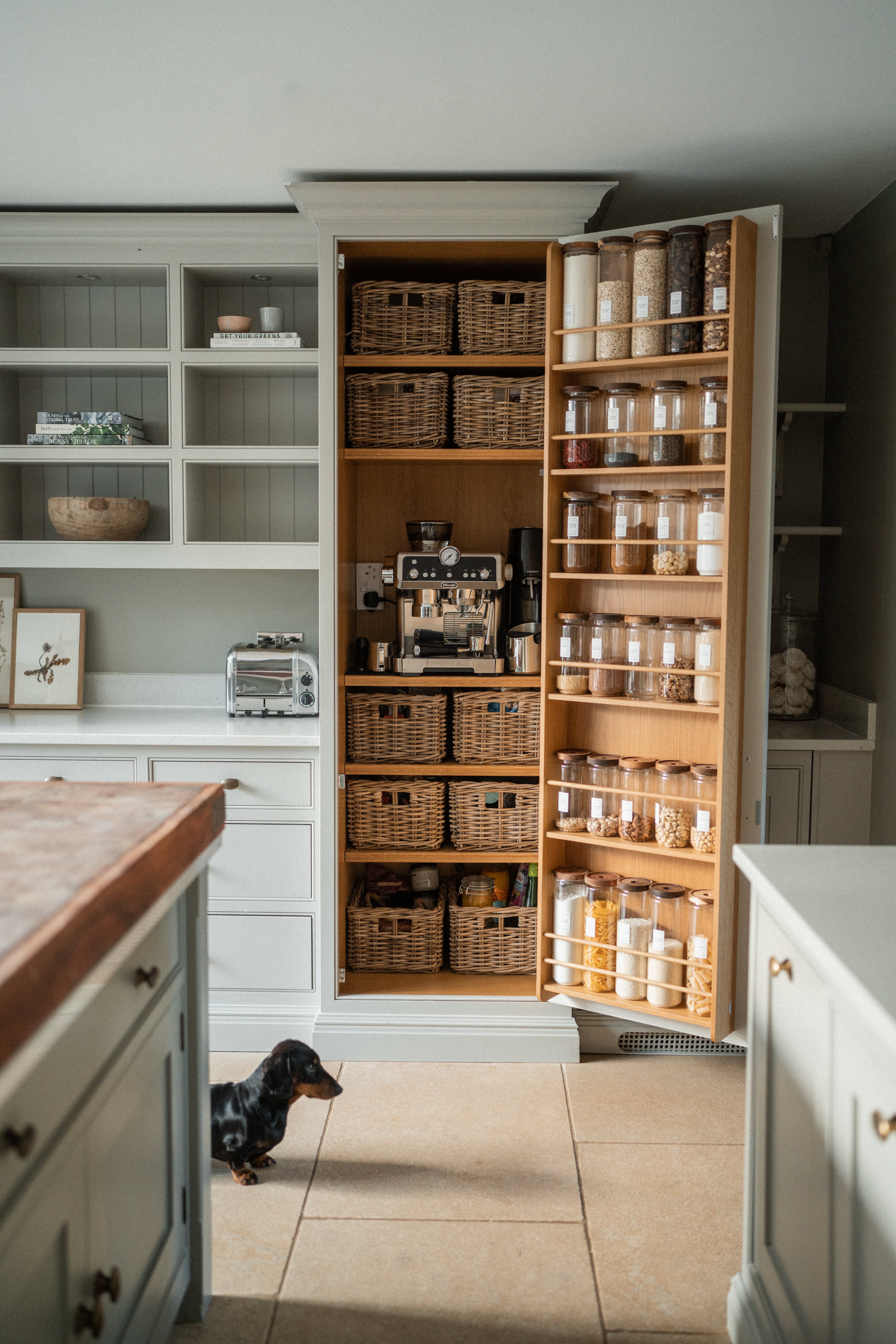 An open pantry door revealing shelves of wicker baskets and a narrow, vertically oriented spice rack filled with various dry…