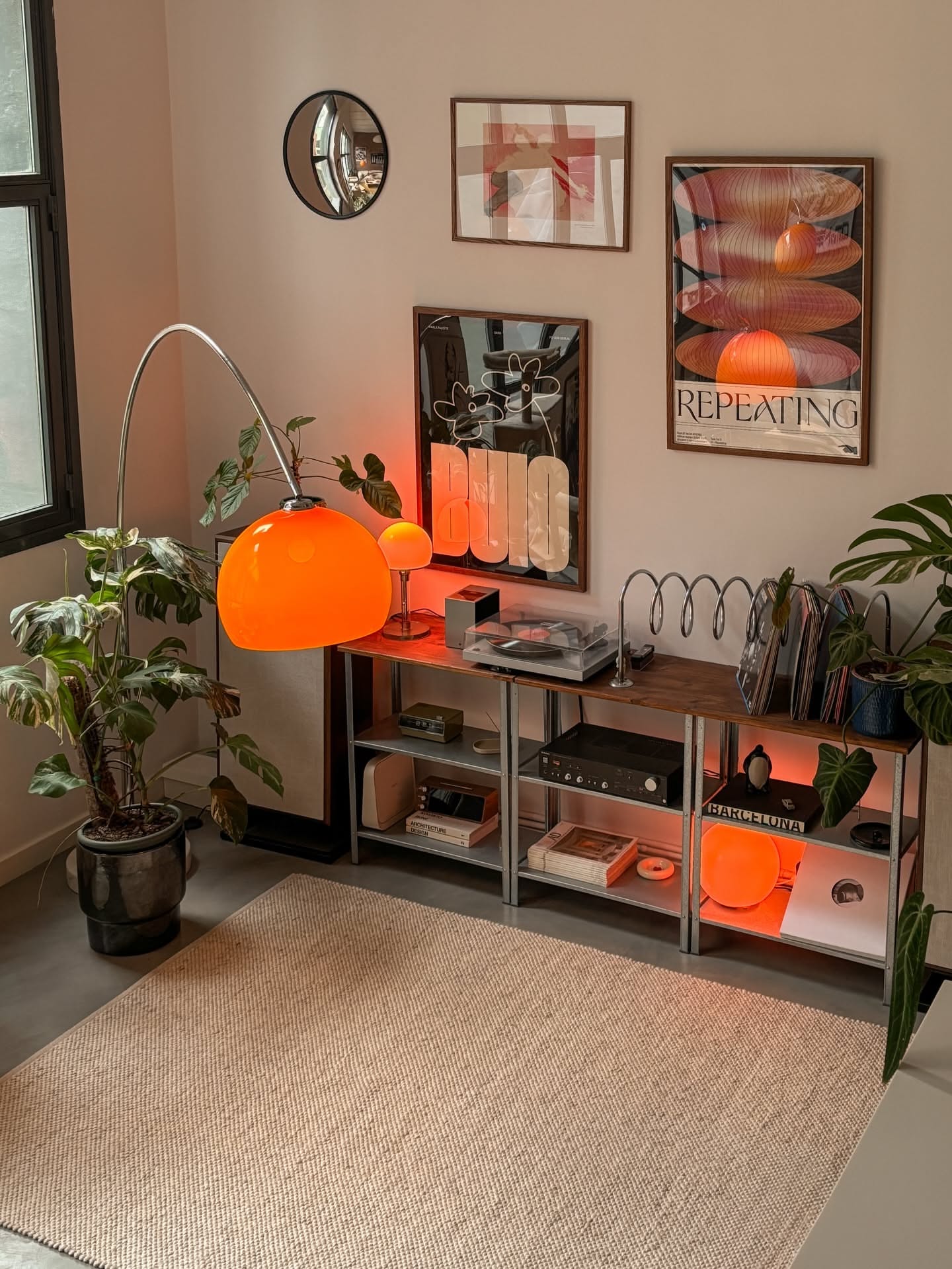 Living room with shelving unit, record player, art prints, large green plant, and bright orange floor lamp