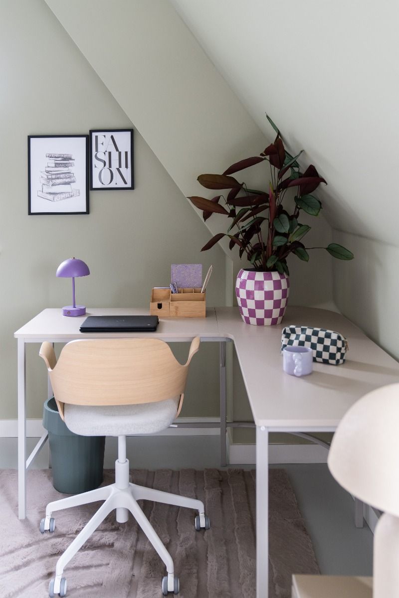 Neutral-toned L-shaped desk with a wooden office chair, a purple lamp, and a large plant in a checkered pot.