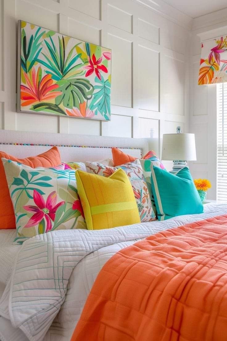 Bedroom with white paneled walls and headboard features a bed with white bedding, an orange bedspread, and colorful tropical…