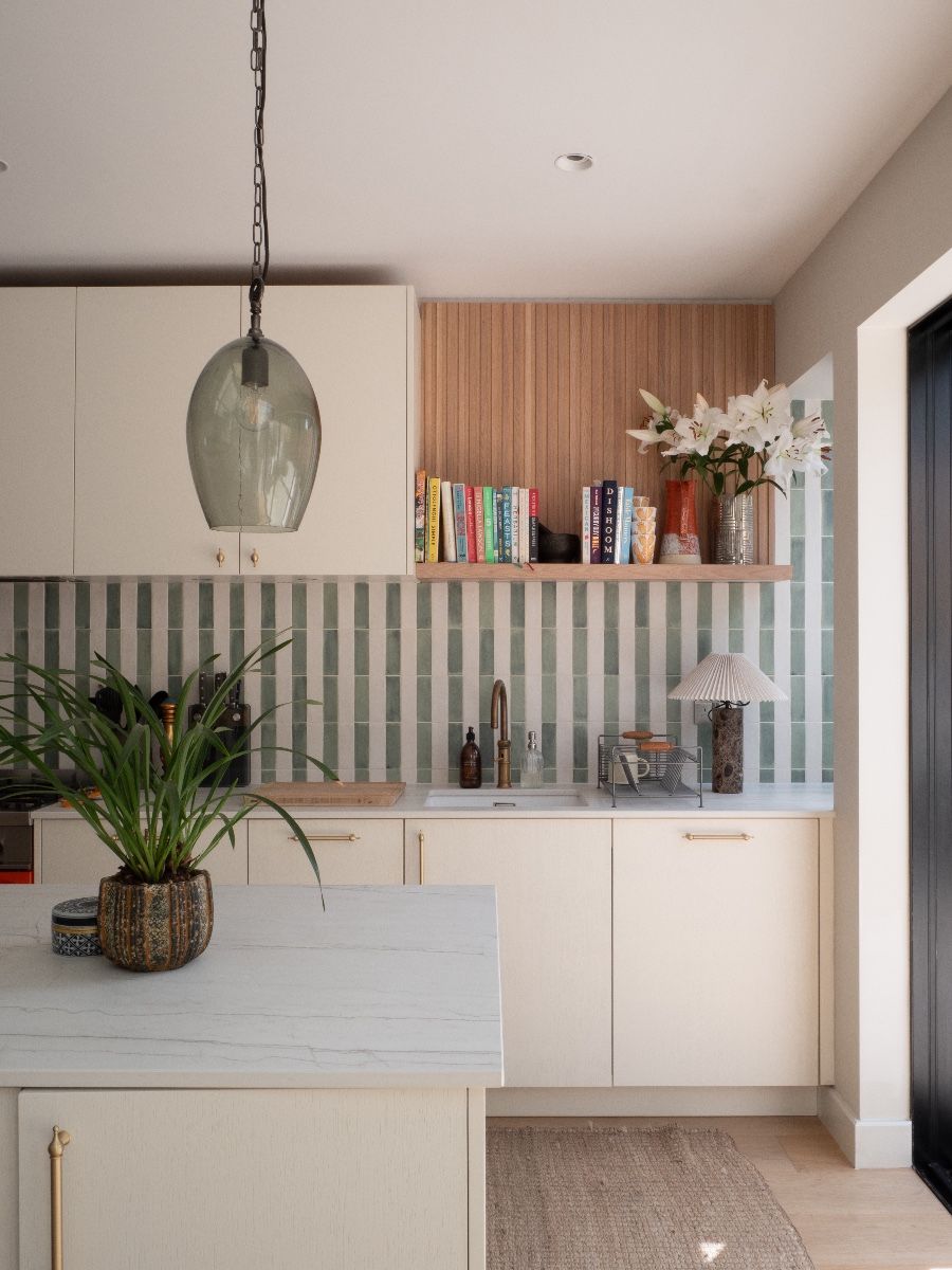 A kitchen with cream-colored cabinets, a white marble island, and green and white striped vertical tiles on the backsplash.