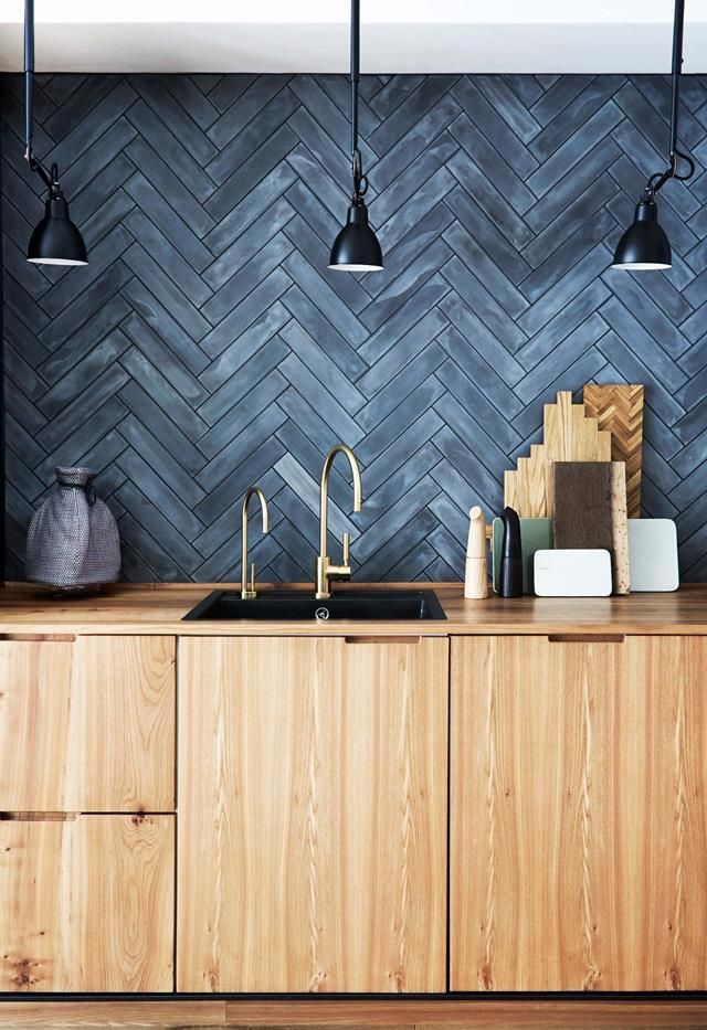 Kitchen with dark gray herringbone backsplash, wood cabinets, black sink, and brass faucets.