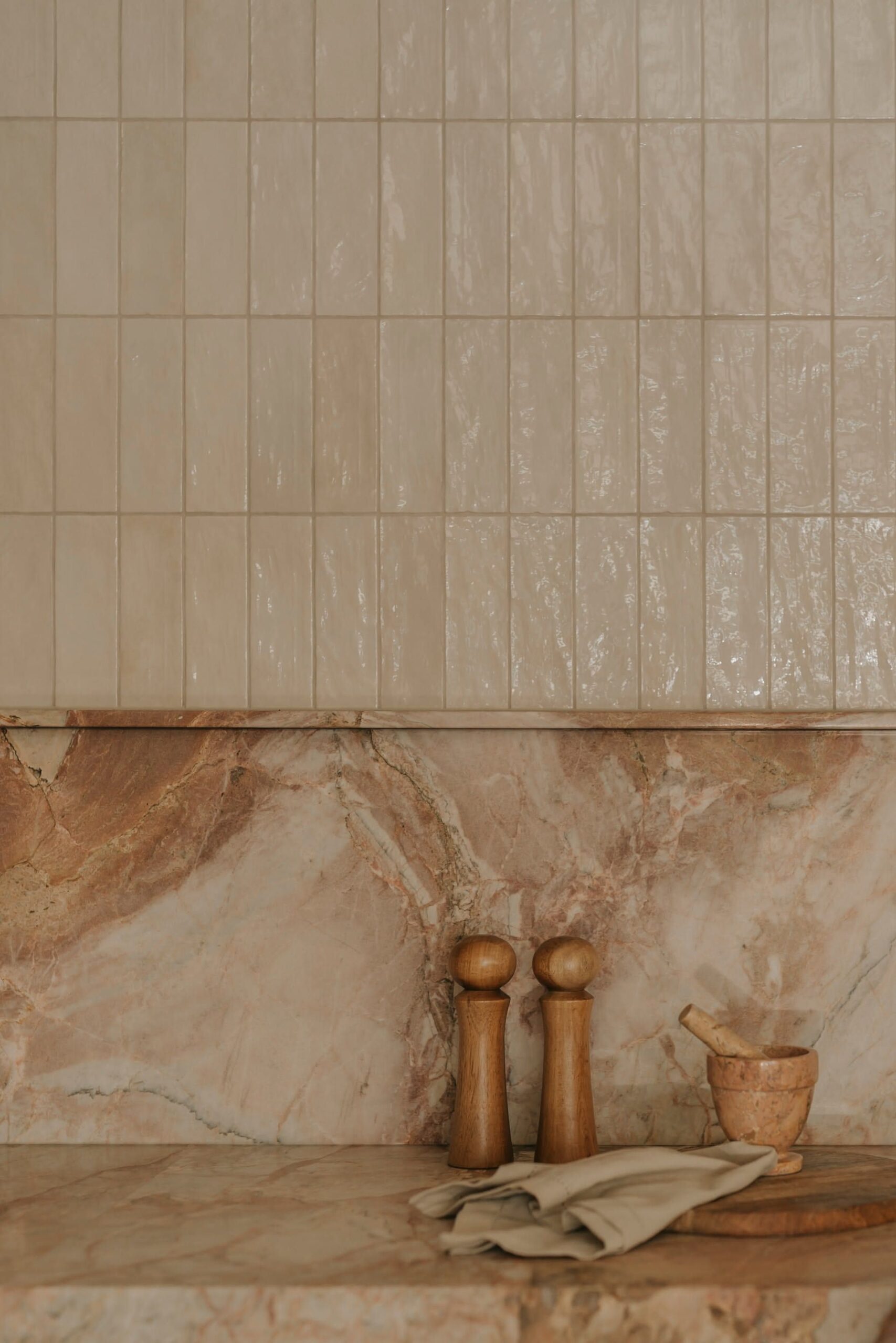 A kitchen counter with a peach-colored marble countertop and backsplash, above which are light tan rectangular tiles.