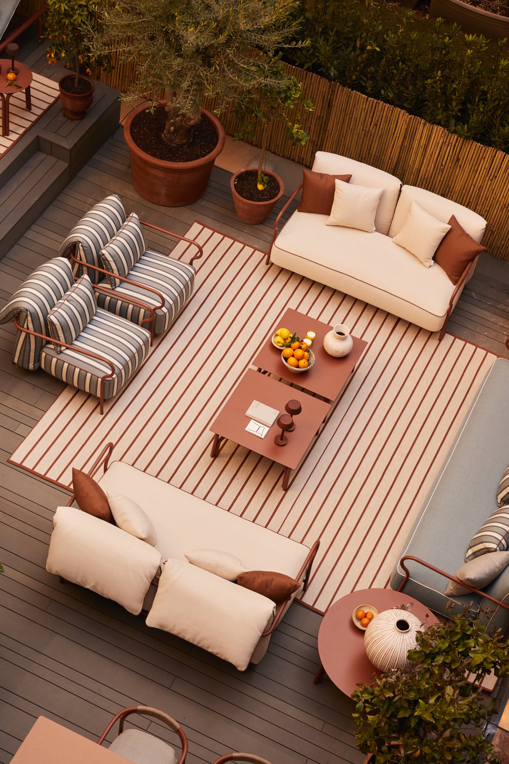 An outdoor living space with two sofas, two armchairs, and two coffee tables. Two large potted plants are present.