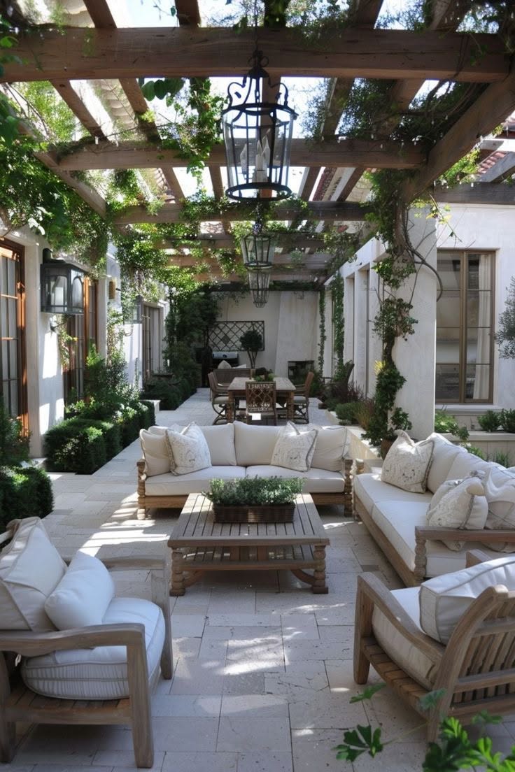 A large outdoor living room and dining area beneath an extensive wooden pergola covered in lush green vines.