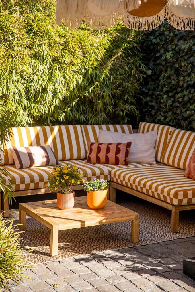 L-shaped outdoor sofa with yellow and white striped cushions on a paved patio with potted plants