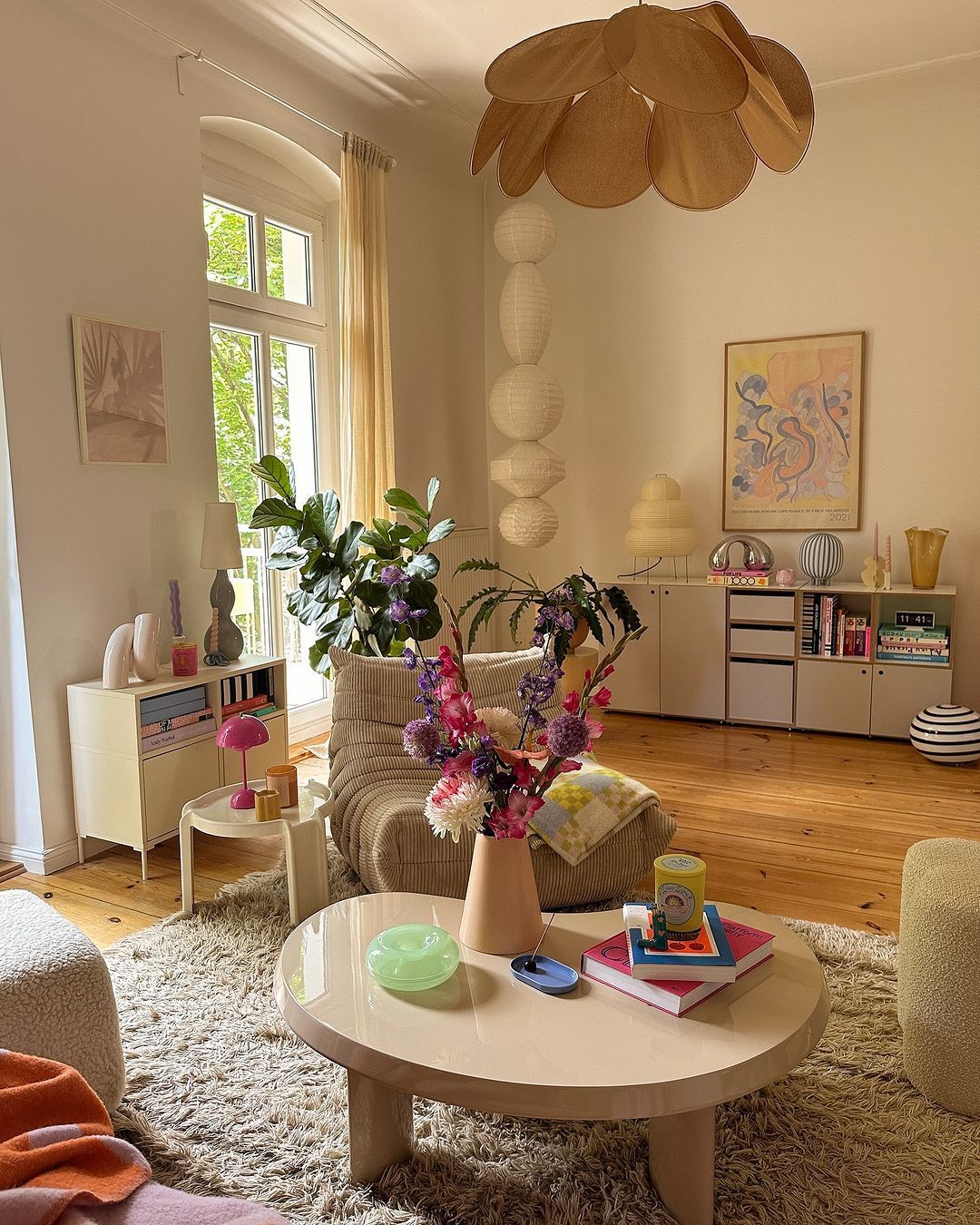 A beige-colored living room with light wooden floors, a shaggy rug, and various pieces of furniture.