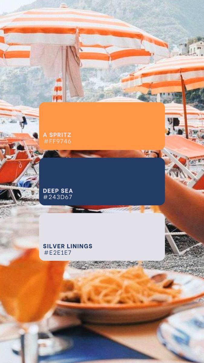 Beach scene with orange and white striped umbrellas, lounge chairs, a glass of spritz, and a plate of pasta on a table.