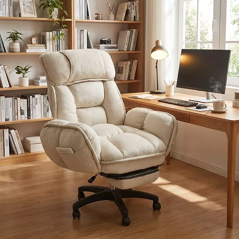 Plush, light-colored ergonomic office chair with a retractable footrest in a home office with a wooden desk and bookshelf.