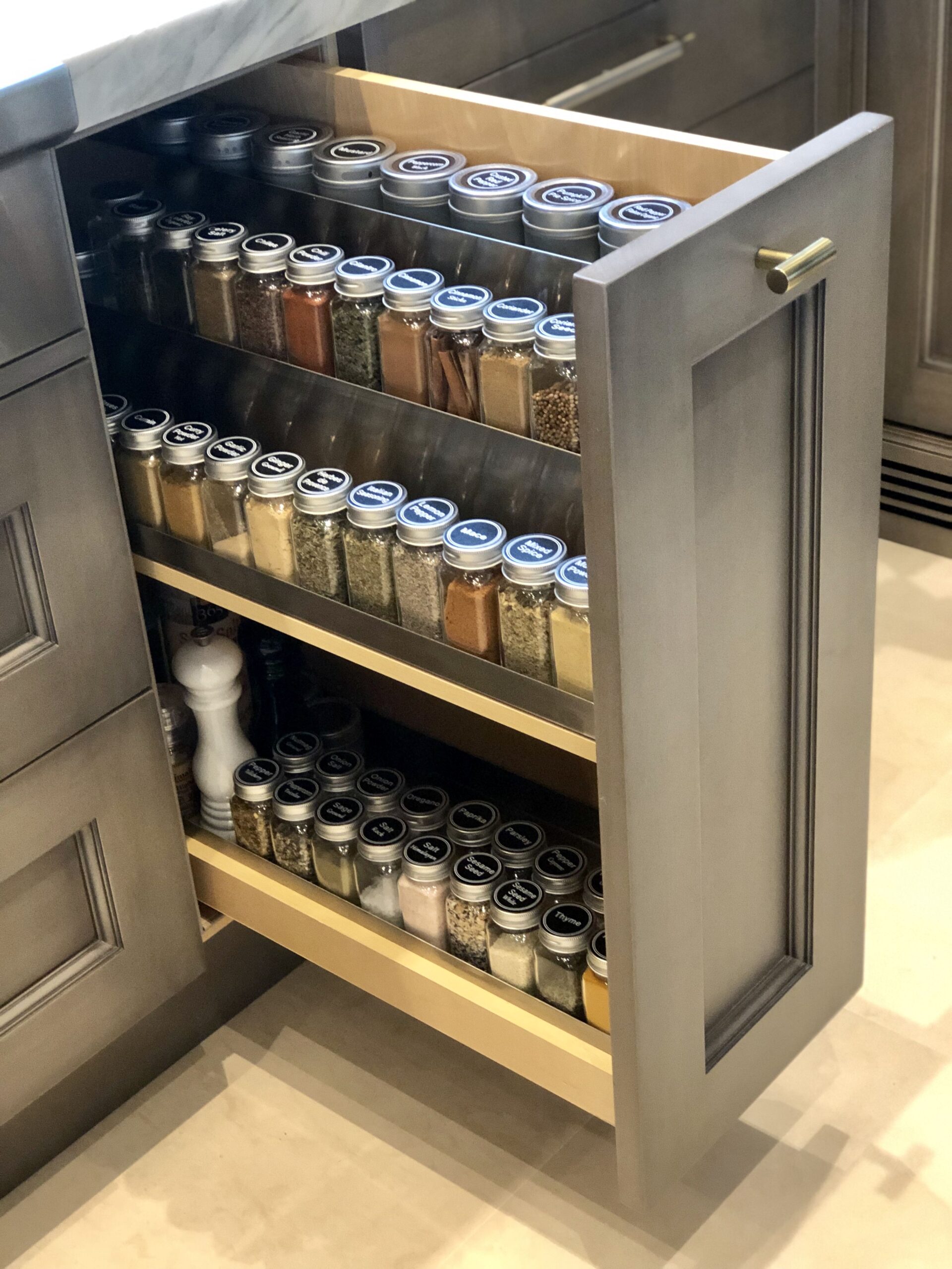 Kitchen cabinet with an open pull-out drawer system filled with neatly organized spice jars and tins.